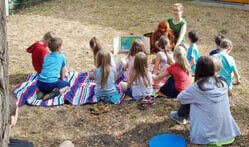 Mehre Kinder einer KiTa schauen sich im Garten das Bildertheater mit Orang-Utan-Handpuppe Ginting an.
