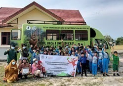 Der Bibliotheksbus vor einer Schule. Auf dem Bild sind viele Kinder, die ein langes Banner halten, sowie einige Erwachsene. Alle winken und schauen in die Kamera.