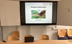 Seminarraum der Universität Leipzig mit Tischen, Stühlen und einer auf einer elektronischen Tafel geöffneten Präsentation.