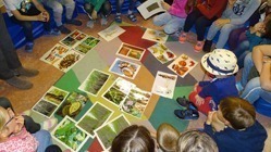 Grundschulkinder sitzen gemeinsam im Kreis auf dem Boden und schauen sich verschiedene Bilder an.