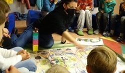 Grundschulkinder sitzen gemeinsam mit unserer Umweltbildnerin im Kreis und schauen sich ein Regenwaldplakat an.