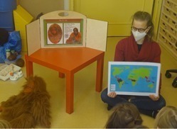 Unsere Umweltbildnerin sitzt mit einer Weltkarte vor einer Gruppe von Kindern.
