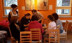 Mehrere Frauen sitzen um einen Tisch. Zwei Umweltbildnerinnen stehen neben ihnen und erläutern etwas.
