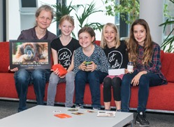 Julia Cissewksi erhält eine Spende von 4 Schülern. Alle sitzen auf einem Sofa und lächeln in die Kamera.
