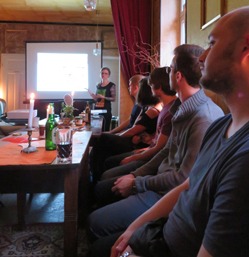 Menschen sitzen an einem Tisch mit Getränken und hören der Präsentation zu.