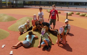 Eine Gruppe Kinder mit selbstgebastelten Papiermasken auf einem Spielplatz.