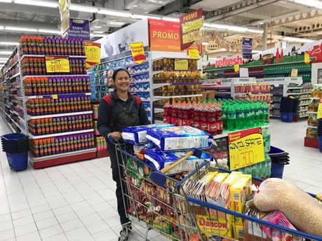 Ibu Maryanti in einem Supermarkt mit einem gefüllten Einkaufswagen.