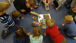 Kinder sitzen im Kreis auf dem Boden. Eine Umweltbildnerin erklärt ihnen etwas.