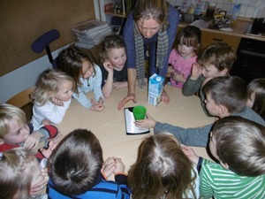 Die Kinder beugen sich in einem Kreis um den Tisch und wiegen gerade etwas auf einer Waage.