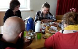 4 Menschen sitzen an einem Tisch, sie trinken Kaffee und diskutieren.