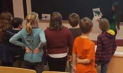 Einige Schüler während des Workshops. Sie stehen vor einer Kreidetafel und hören der Umweltbildnerin zu.