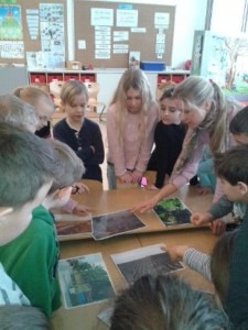 Eine Gruppe Kinder steht um einen Tisch mit Fotos und redet über diese.