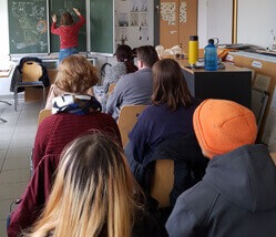 BFDler im Klassenzimmer beim BFD-Seminar. Jemand schreibt vorne etwas an eine Kreidetafel.