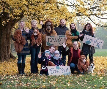 Ein Gruppenfoto einiger unserer Vereinsmitglieder mit kleinen Plüsch-Orang-Utans in einem Park. Drei der Mitglieder halten Dankesschilder in die Kamera. Alle lächeln. Ein Mitglied trägt ein Orang-Utan-Kostüm.