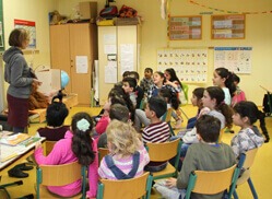 Kinder sitzen in einem Stuhlkreis und hören einem Vortrag zu.