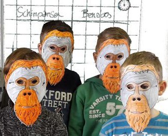 Vier Grundschulkinder mit selbstgebastelten Orang-Utan-Masken schauen in die Kamera.