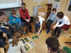 Kinder sitzen in einem Stuhlkreis und reden über ausgedruckte Bilder auf dem Fußboden.