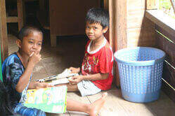 Two Indonesian children holding education materials look into the camera.