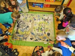 Kinder schauen sich ein auf dem Boden liegendes Poster mit vielen Tieren des Regenwaldes an.