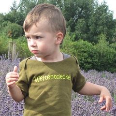 Ein Kind steht in einer Lavendelwiese und schaut zur Seite. Auf dem T-Shirt steht Weltentdecker.