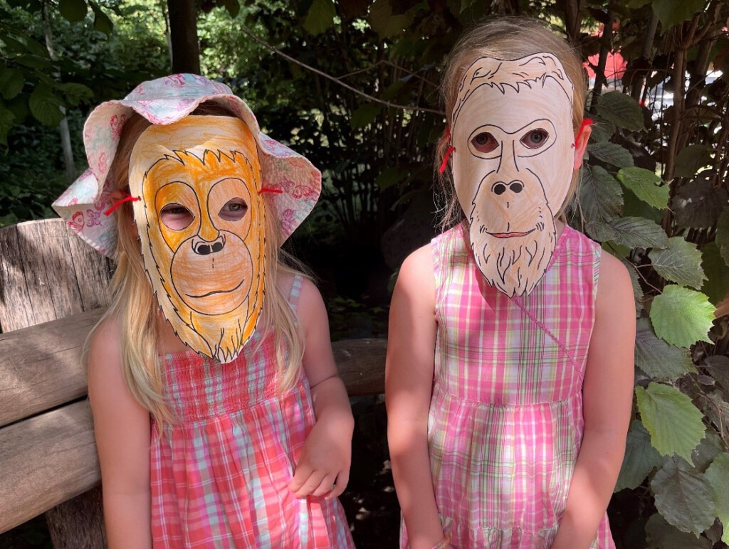 Zwei Mädchen mit selbstgebastelten Orang-Utan-Masken schauen in die Kamera.