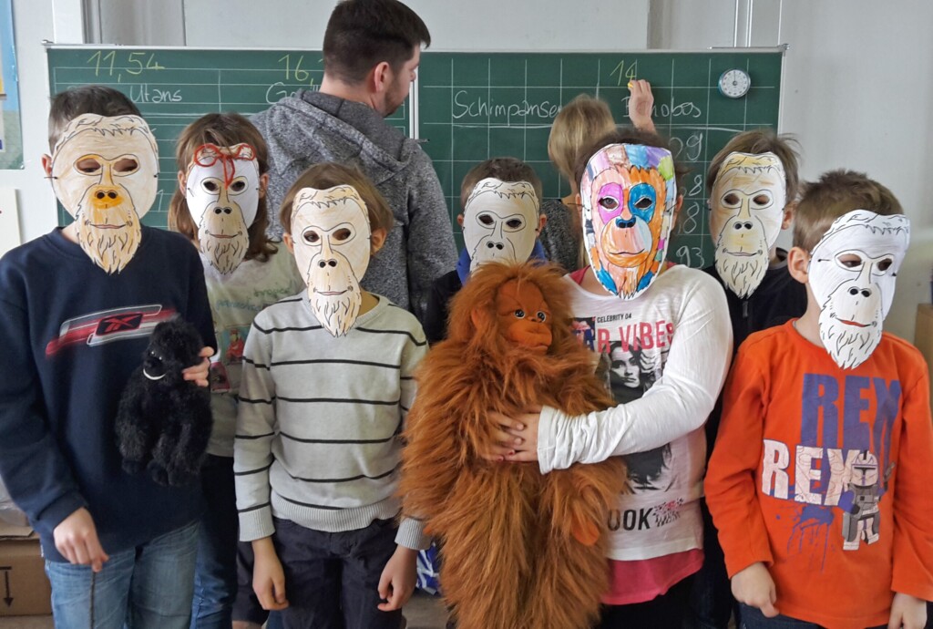 Gruppenfoto: Eine Gruppe Grundschüler mit selbstgebastelten Orang-Utan-Masken im Klassenraum.