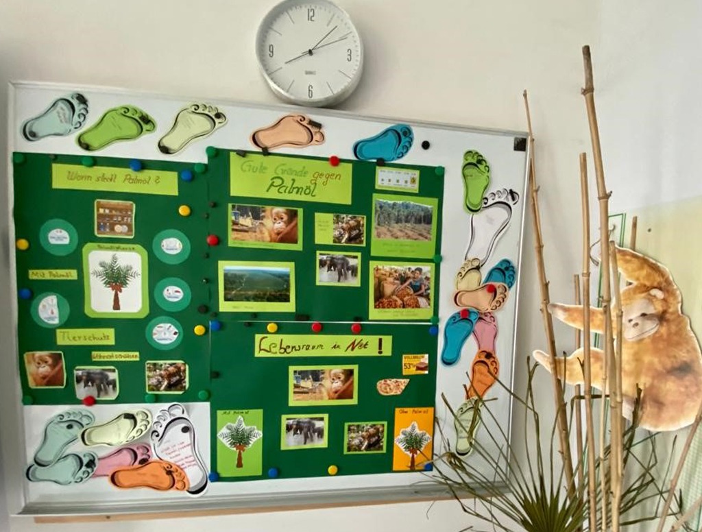 Poster zum Thema Palmöl hängen an einer Tafel. Darum sind Fußabdrücke aus Papier verteilt, auf die von den Schülern Maßnahmen zum Umweltschutz geschrieben wurden.