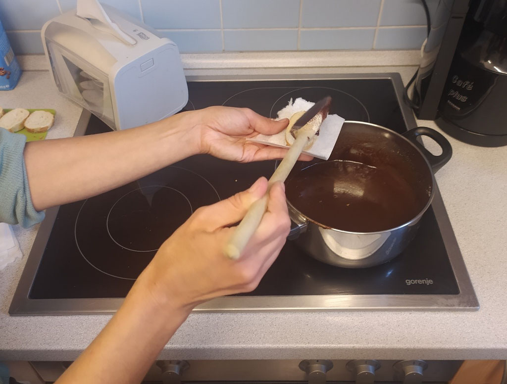 Selbst hergestellter palmölfreier Schokoaufstrich steht in einem Topf auf dem Herd. EIne Umweltbildnerin streicht etwas davon auf ein Stück Brot zum Kosten.