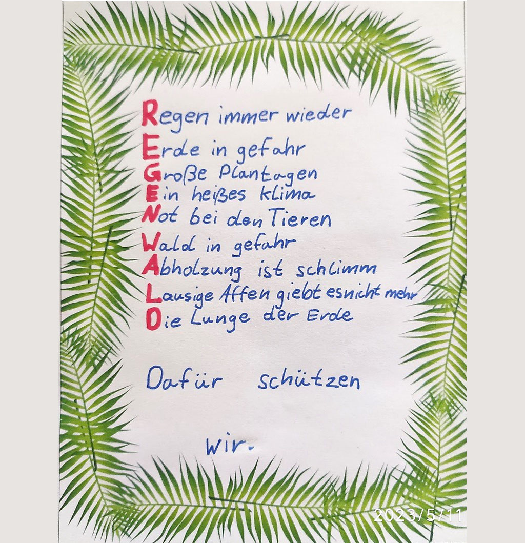 Auf einem Stapel von Arbeitsblättern liegt ein Gedicht über den Schutz des Regenwaldes. Das Gedicht lautet: Regen immer wieder; Erde in Gefahr; Große Plantagen; Ein heißes Klima; Not bei den Tieren; Wald in Gefahr; Abholzung ist schlimm; Lausige Affen gibt es nicht mehr; Die Lunge der Erde; Dafür schützen wir. Die Anfangsbuchstaben jeder Zeile sind rot hervorgehoben und ergeben das Wort „Regenwald“.