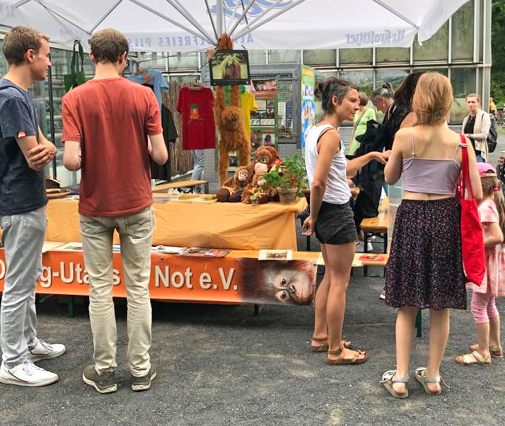 Besucher des Sommerfestes stehen vor unserem Infostand und führen Gespräche mit Unterstützern des Vereins.