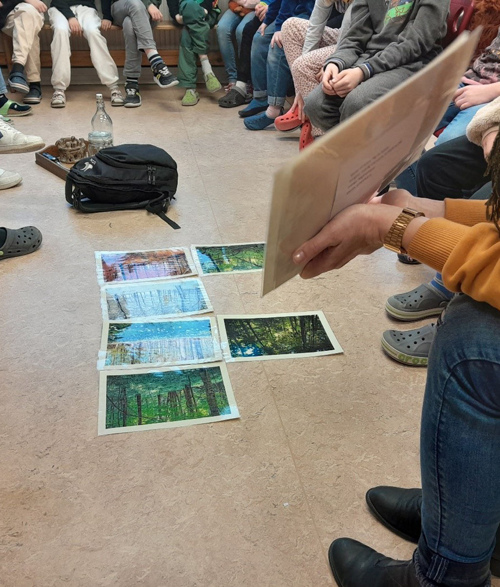 Eine Gruppe von Schülerinnen sitzt im Kreis, auf dem Boden liegen Bildkarten.