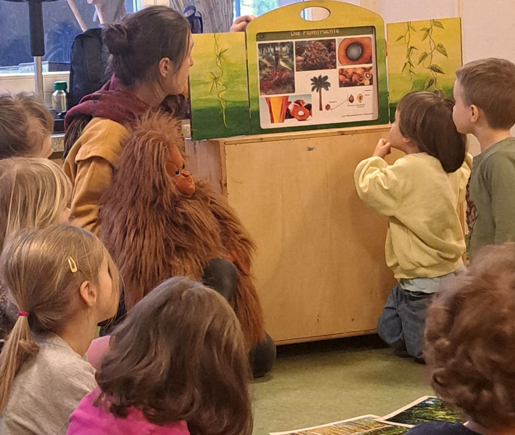 Umweltbildnerin mit Orang-Utan-Handpuppe vor einem Erzähltheater, im Vordergrund und am Bildrand sind Kinder zu sehen.