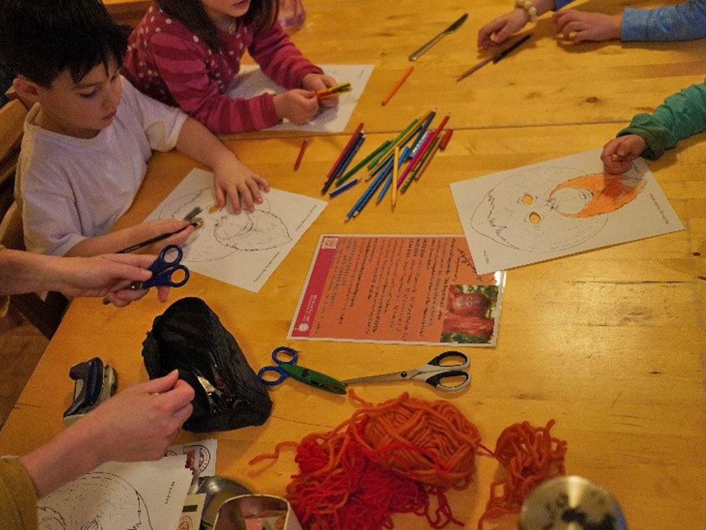 Kinder sitzen an einem Tisch, auf dem Orang-Utan-Masken, Stifte, Scheren und Wolle liegen.