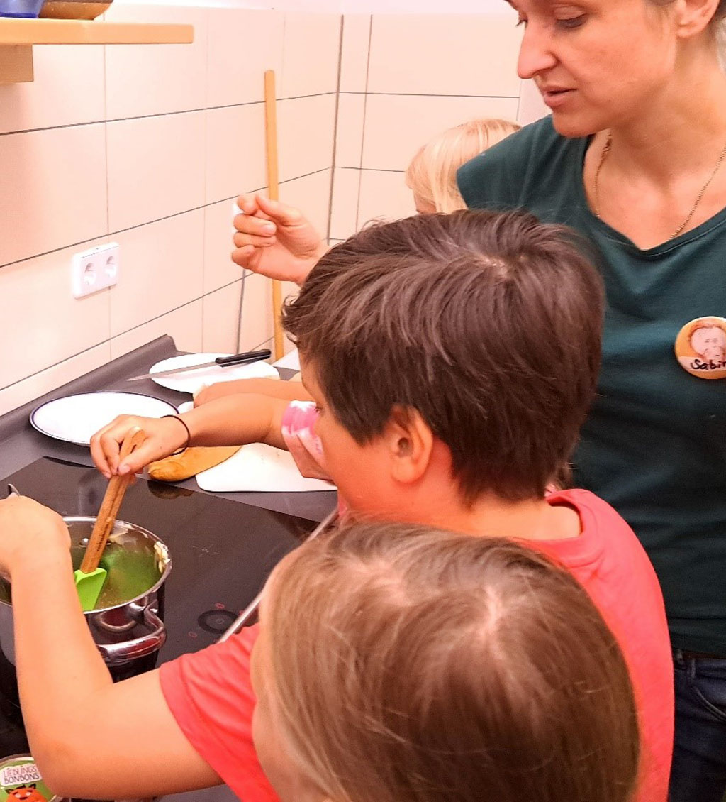 Mehrere Kinder und die Umweltbildnerin stehen am Herd. Ein Kind rührt in einem Topf.