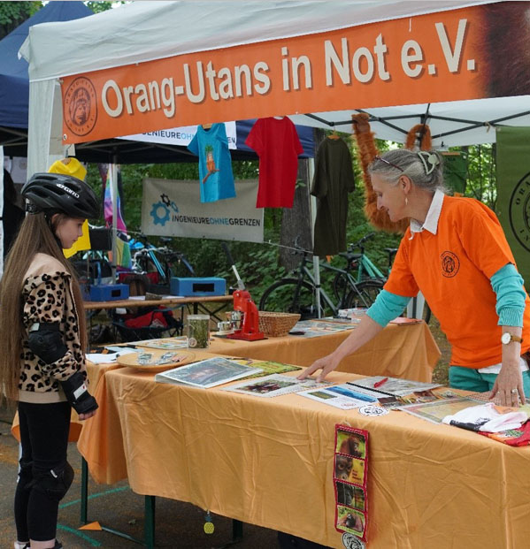 Am Informationsstand des Orang-Utans in Not e.V. steht ein Kind, eine Frau präsentiert Informationsmaterial.