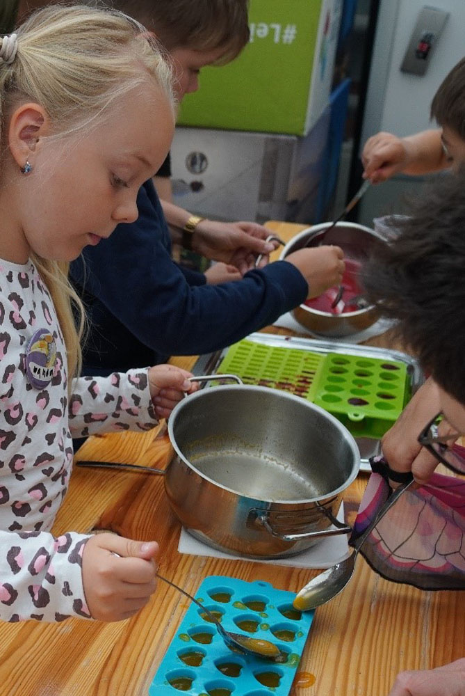 Mehrere Kinder füllen farbige Flüssigkeit in Eiswürfelsilikonförmchen.