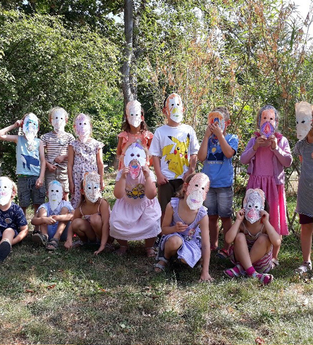 Zwei Reihen Kinder sitzen bzw. stehen auf einer Wiese. Alle Kinder tragen bunte Orang-Utan-Masken aus Papier