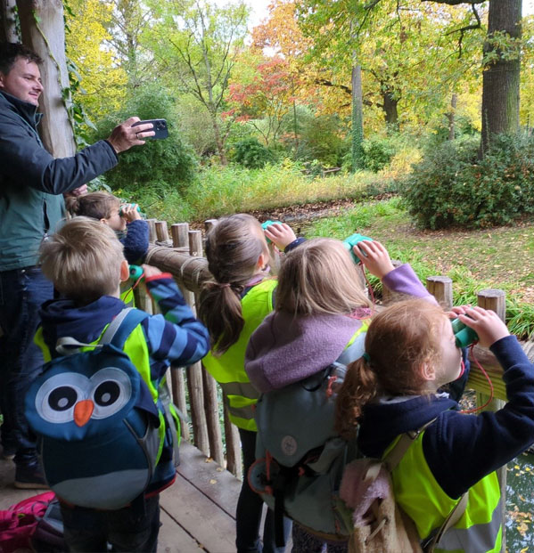 Fünf Kinder schauen im Zoo durch Ferngläser auf das Außengehege der Orang-Utans.