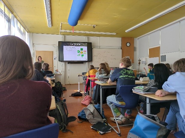 Die Umweltbildnerin steht vor einer Schulklasse im Klassenzimmer und erklärt etwas.