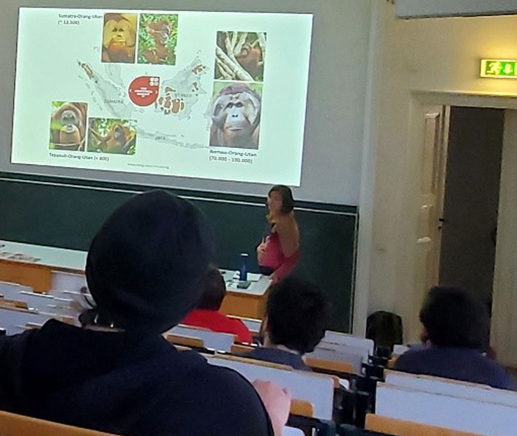 In einem kleinen Hörsaal sitzen Studierende. Die Umweltbildnerin steht an einer Tafel. Darüber wird eine Präsentation an die Wand projiziert.