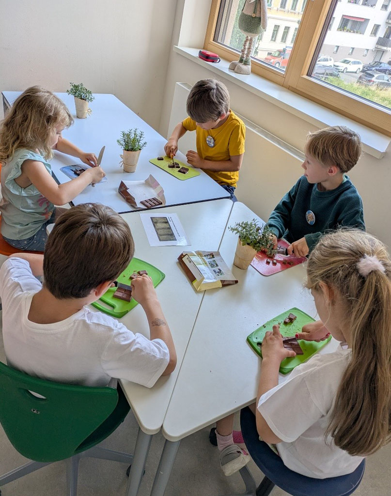 Fünf Kinder sitzen um einen Tisch herum und schneiden Schokolade klein.