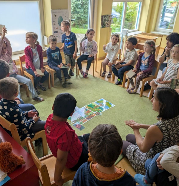 Kinder sitzen im Kreis auf Stühlen. In der Mitte liegen Bildkarten auf dem Boden.