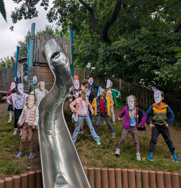 Kinder stehen rechts und links von einer Rutsche. Sie tragen bunte Orang-Utan Masken.