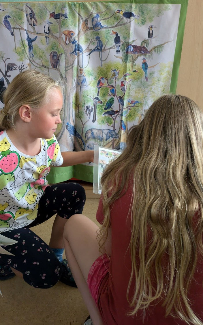Zwei Kinder hocken vor einem Plakat mit Regenwaldtieren.