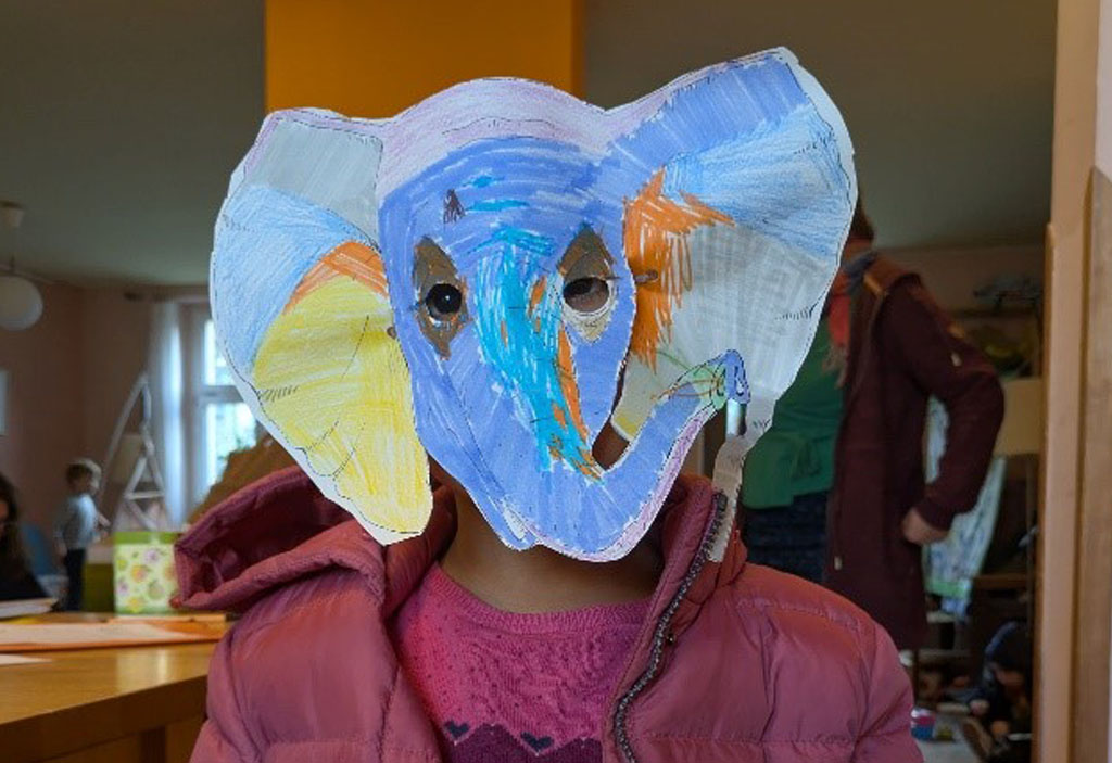 Ein Kind trägt eine bunt bemalte Elefantenmaske.
