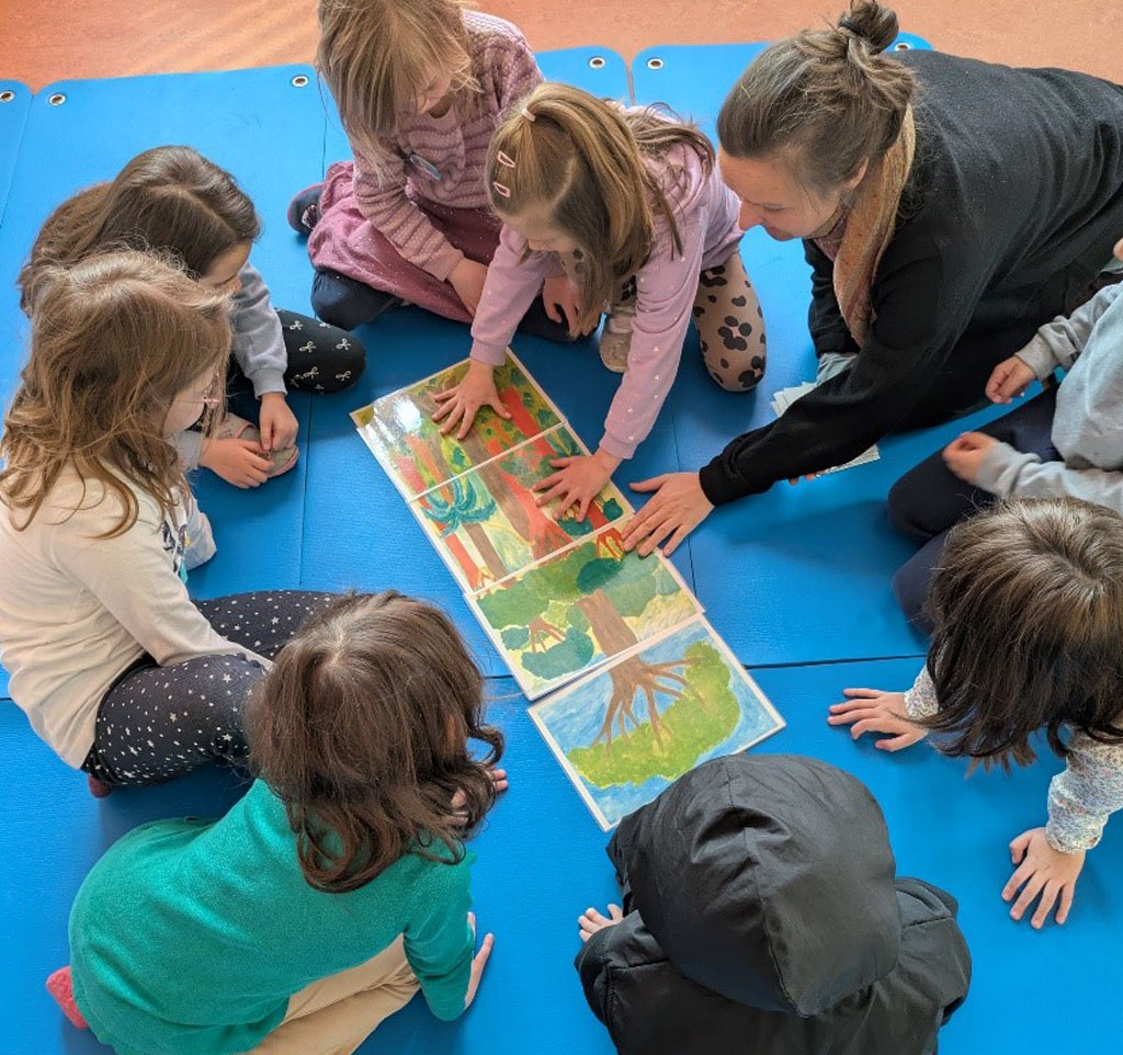 Kinder sitzen auf blauen Matten und puzzeln ein Regenwaldbild zusammen. Die Umweltbildnerin unterstützt sie dabei.
