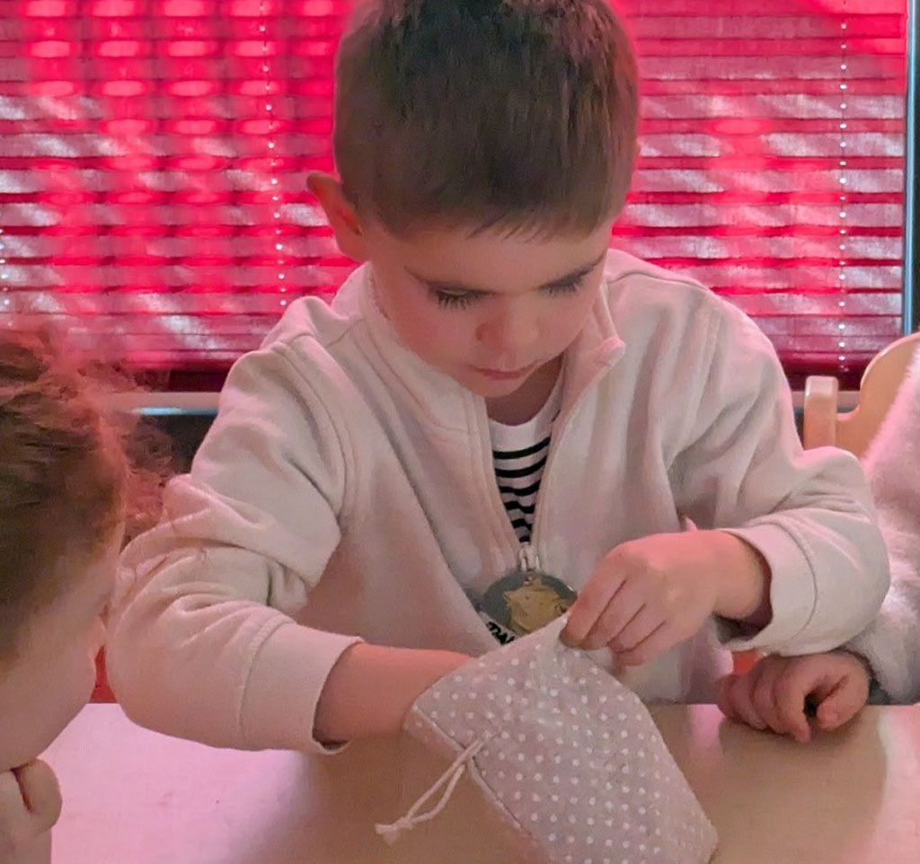 Ein Kind sitz vor einer pinken Jalousie und steckt seine Hand in ein Fühlsäckchen.