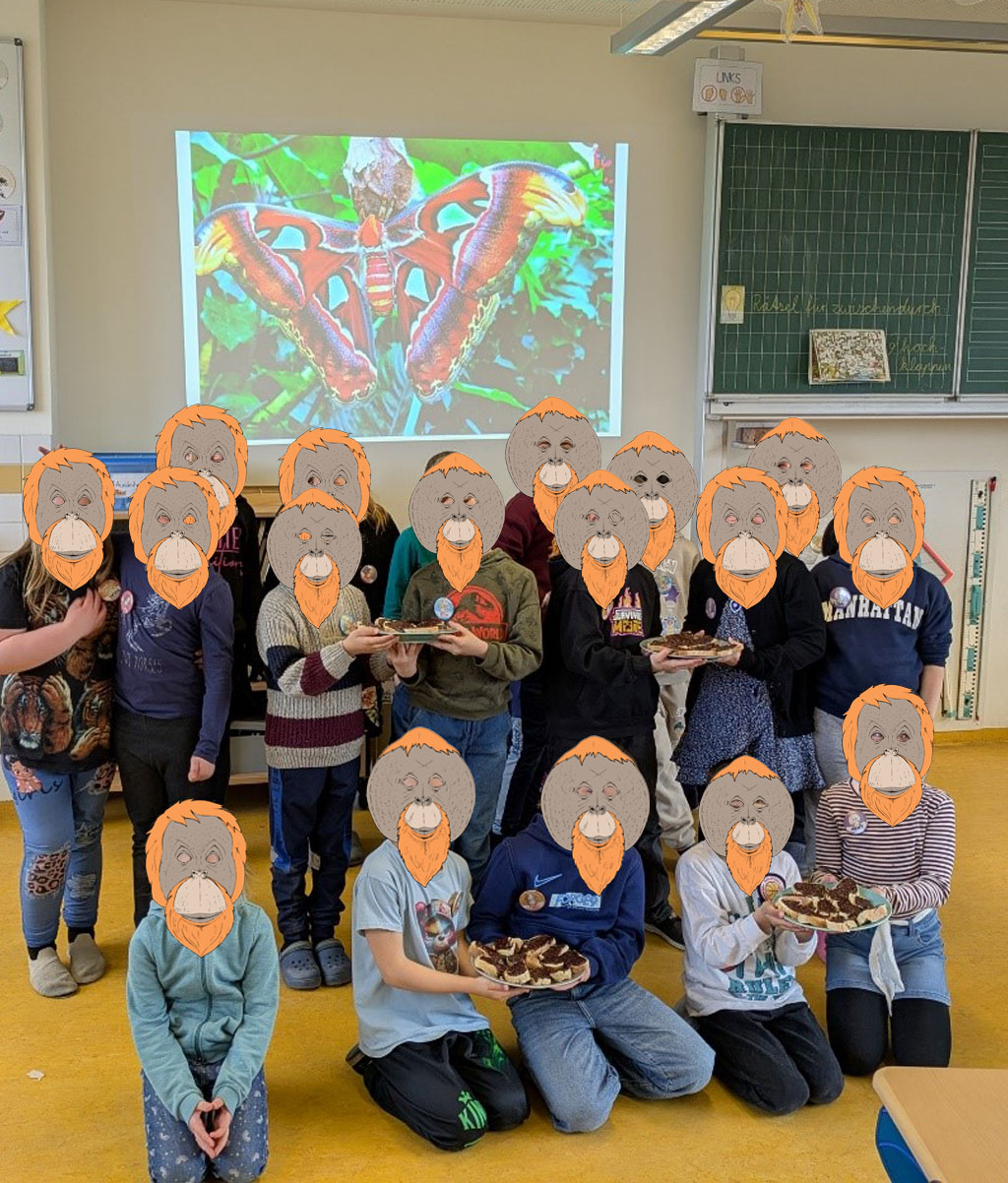 Eine Klasse steht vor der Projektion eines Altlasspinners. Ein paar Kinder halten Teller in den Händen auf denen Schokoladenbrote liegen.