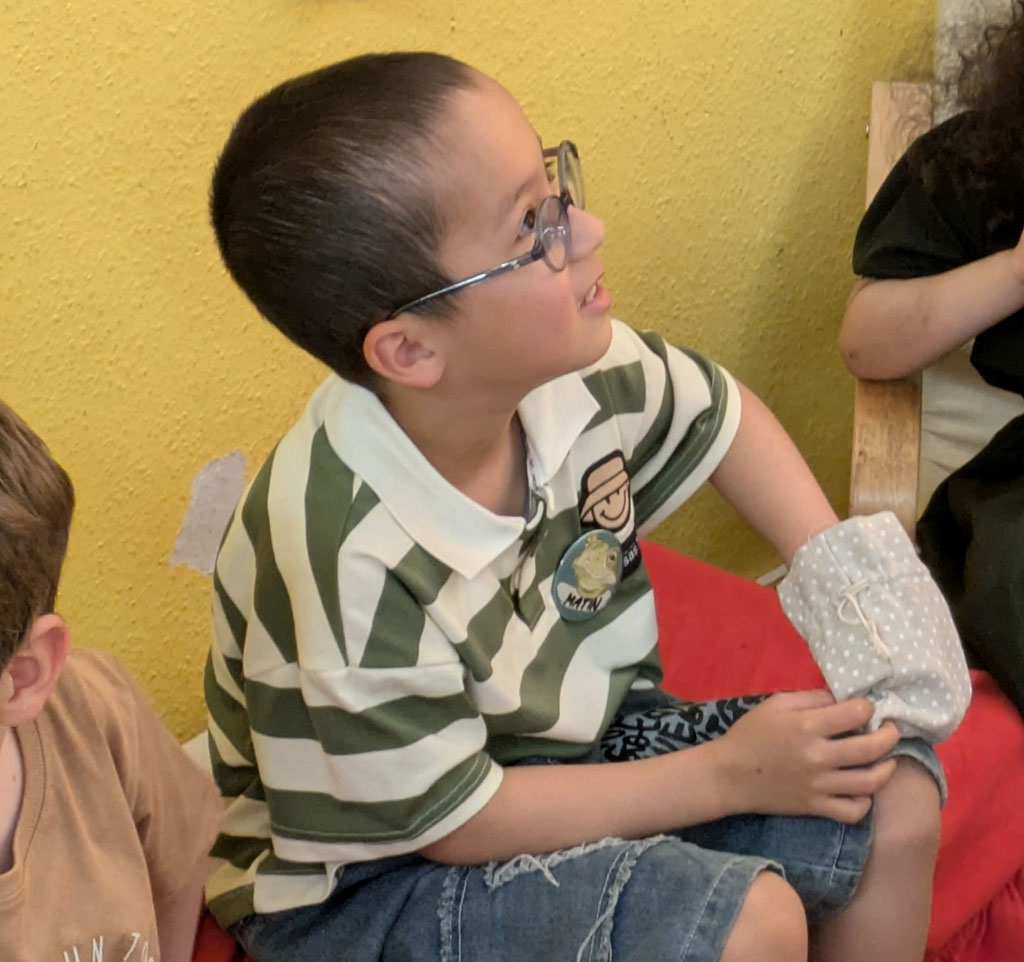 Ein Kind steckt seine Hand in ein kleines Säckchen. Recht und links von ihm sitzen weitere Kinder.