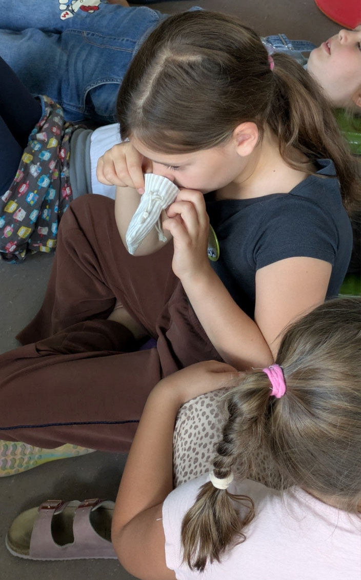Ein Kind riecht an einem kleinen Säckchen. Links und rechts von ihm sitzen weitere Kinder.